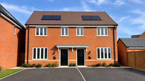 A two-story red brick semi-detached house with black doors and solar panels sits behind a paved driv