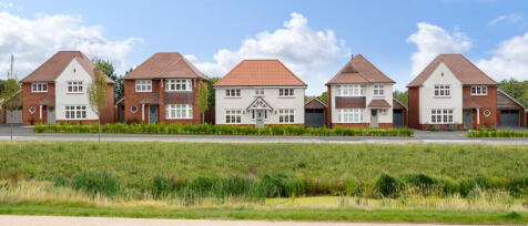 A row of modern detached houses with red brick and white exteriors, set against a partly cloudy sky