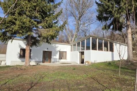 Exterior view of the renovated Bulgarian house showing white walls, large windows, and surrounding trees