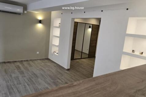View of kitchen with wooden countertop and adjoining room, both with tiled floors.