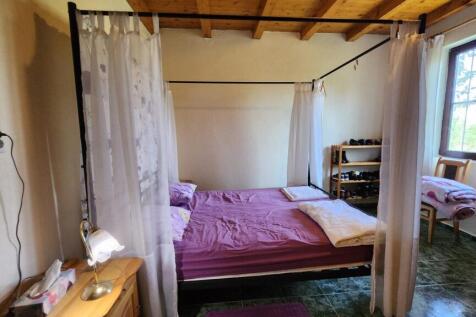 Bedroom interior featuring a four-poster bed with purple bedding, wooden ceiling beams, window with curtains, and shoe rack