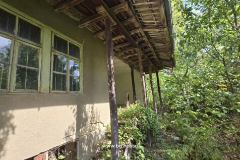 Traditional Bulgarian house exterior showing wooden roof supports and surrounding greenery.
