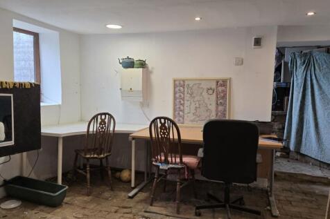 Interior room containing desks, chairs, and a framed map on the wall under two windows.