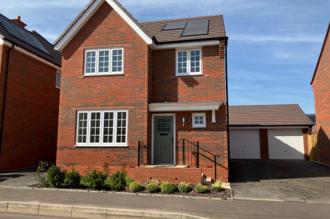 A modern red brick house with white-framed windows and solar panels on the roof stands in the foregr
