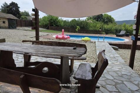 Rustic wooden benches and table on stone patio overlooking a swimming pool with wooden decking.