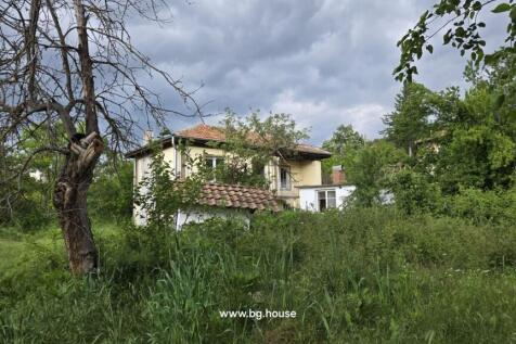 Two-storey yellow house with tiled roof surrounded by tall grass and trees in the garden.