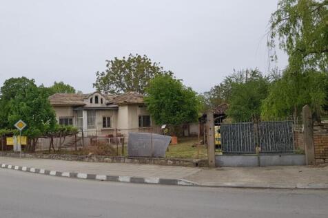 View of a single-storey house with a tiled roof surrounded by a wire fence and trees on a street corner