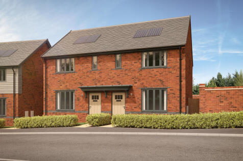 A row of modern brick houses with manicured hedges in the foreground sits under a bright blue sky wi