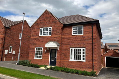 A modern red brick house with white-framed windows and a dark front door stands on a paved driveway