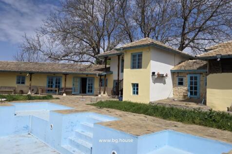 Yellow rural house with blue doors and windows beside an empty blue swimming pool