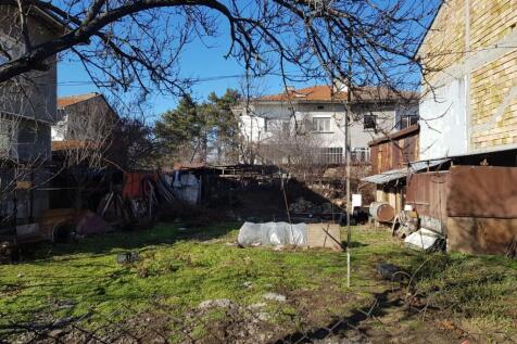Grassy fenced land featuring garden beds and bare trees beside brick and plaster buildings in Popovo