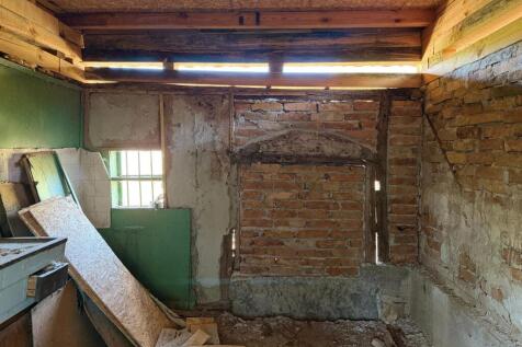 Interior space featuring an exposed brick wall, wooden ceiling beams, and scattered construction materials on the floor.