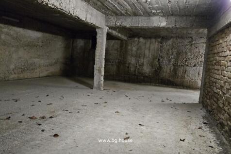 View of an unfinished basement featuring concrete walls and ceiling, a brick wall on one side, and a central supporting pillar.