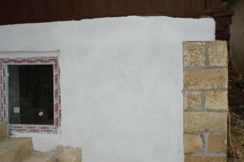 White plastered exterior wall section with a stone corner and a window with protective film.