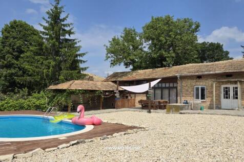 View of the house exterior featuring a round swimming pool with inflatables and a shaded seating area beside the house.