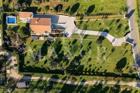 Bird's-eye drone view of a brand new luxury villa for sale in Algarve, showcasing the private swimming pool, spacious garage, and sprawling 10,000 sqm landscaped plot near Estômbar.