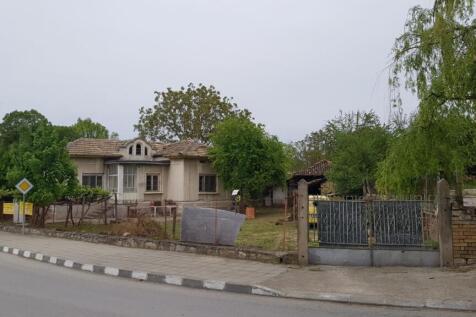 View of a single-storey house with a tiled roof surrounded by a wire fence and trees on a street corner