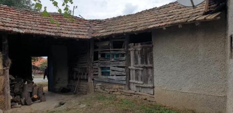 Covered passageway showing a wooden barn wall, firewood stack, and an open gate leading to the street.