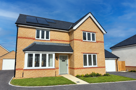A modern two-story brick house with solar panels stands on a green lawn against a clear blue sky.