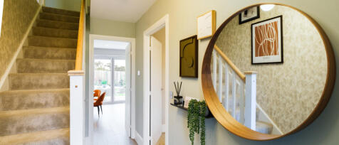 Redrow bright open hallway with large hanging mirror and soft carpeted stair case at Oakleigh Fields
