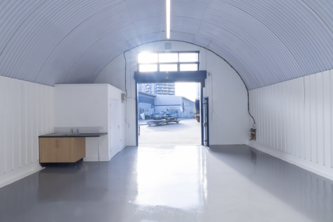 An empty arch with lining, facing the front electric roller shutter entrance, which is open. There is a WC cubicle at the front of the unit.