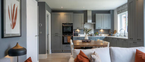 Modern open-plan kitchen and living room with grey cabinetry, wooden dining table, and soft furnishi