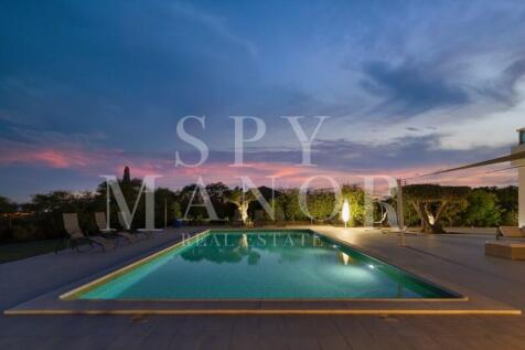 Illuminated swimming pool at a luxury villa in Caramujeira, Algarve. Features a calm water surface reflecting the evening clouds, a poolside deck, and a vibrant twilight sunset sky.