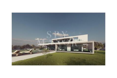 Modern luxury villa for sale in Carvoeiro, Algarve. Showing contemporary white architecture, floor-to-ceiling glazing, outdoor living spaces, pool deck, and landscaped gardens.