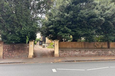 Tree-lined entrance with stone pillars and a ga...