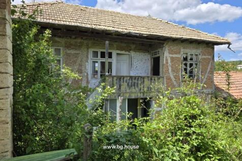 Two-storey brick house with external wooden stairs and broken windows surrounded by plants