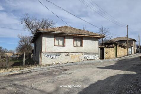 Front view of a Bulgarian village house with a tiled roof and two windows overlooking a quiet dirt road.