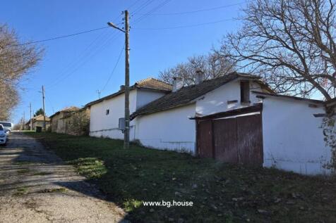 Street scene in village showing white houses with garages and parked cars along the road.