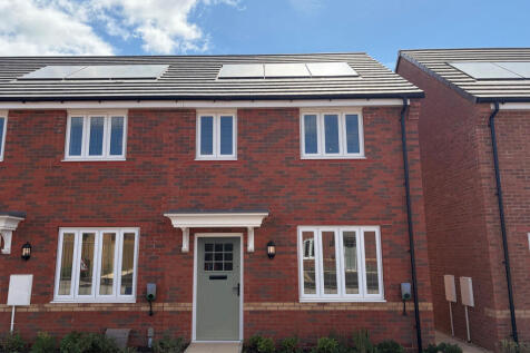 A modern red brick house with white-framed windows and a light green door stands in the foreground