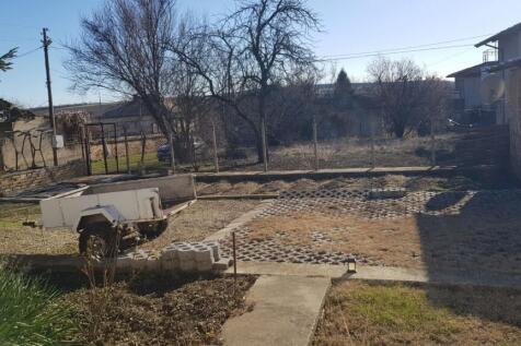 View of garden yard showing paved and grassy areas, a small trailer, and fenced perimeter with trees and nearby houses