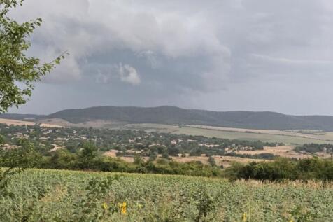 Scenic view over cultivated fields and village houses with rolling hills in the distance under a partly cloudy sky.