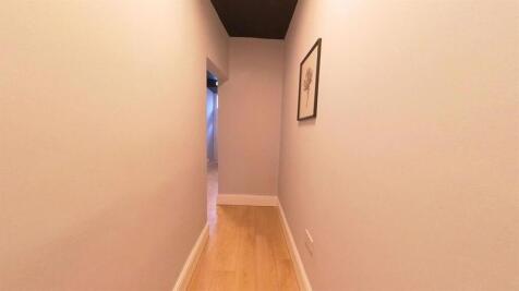 A clean, narrow hallway with light wood floorin...