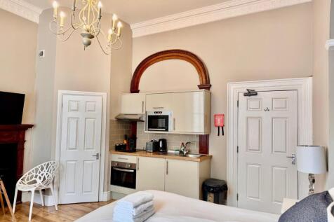 Well-lit room with kitchenette and decorative a...