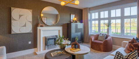 Modern living room with large window, cosy armchair, decorative wall art, and a fireplace with a whi