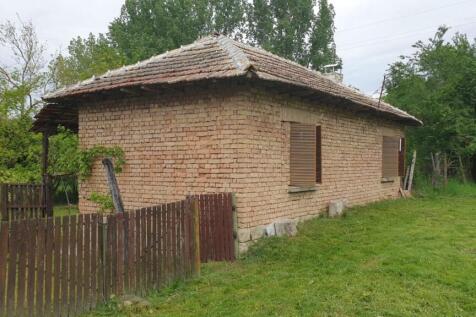 Side perspective showing brick walls, wooden shutters, and a wooden fence enclosing part of the garden