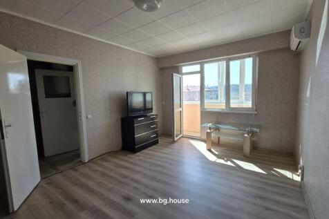Bright living room featuring light wood flooring, patterned wallpaper, a TV on a black chest of drawers, and an open door leading to the balcony.