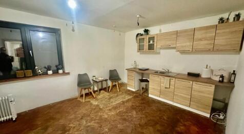 Room featuring wooden flooring, kitchen cabinets, a window, and a door leading to another room.