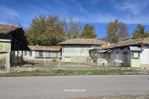 Front view of a traditional Bulgarian house with multiple tiled roofs and a fenced yard in Kovachevets village