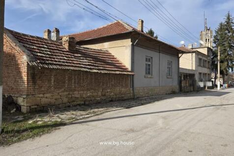 The house with a tiled roof stands beside a quiet road, with a clock tower visible further down the street.