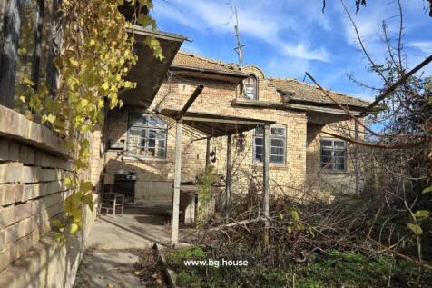 View of the brick house exterior featuring a tiled roof and a covered porch with outdoor furniture and dry vegetation