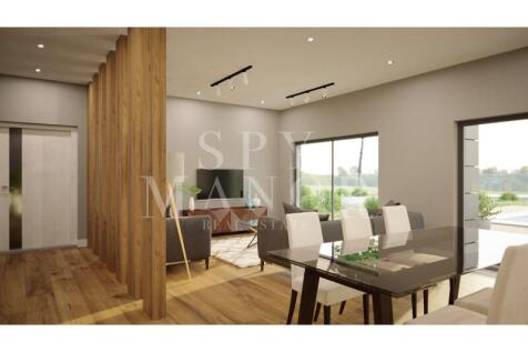Modern dining room and lounge area inside a luxury Algarve villa, showcasing wooden flooring, contemporary dining set, and large glass doors looking out to the garden.
