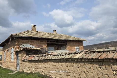 Outside view of a traditional Bulgarian brick house with a tiled roof and stone wall in front