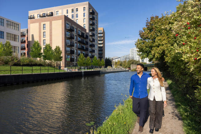 Two people walking down the canal with their arms around each other and the apartments in the distan