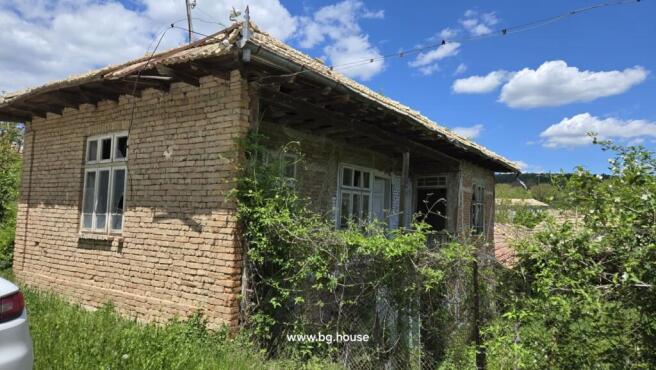 Old brick house with tiled roof and white framed windows surrounded by greenery in Osikovo village