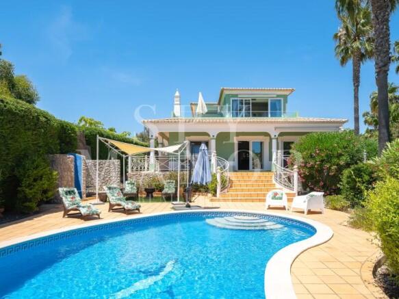 Luxury coastal estate in Carvoeiro, Algarve, featuring a large private swimming pool, sun loungers, and expansive sun-drenched terraces leading to a traditional Algarvian style villa.