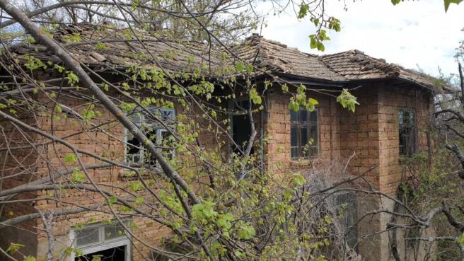 Exterior view of an old brick house with a tiled roof surrounded by leafing trees